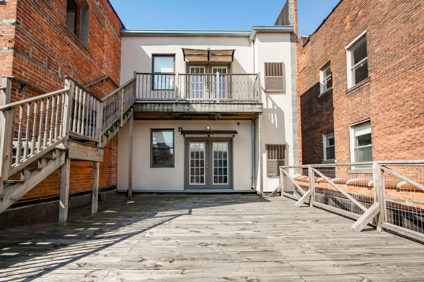 Rear deck with wooden stairs between brick buildings